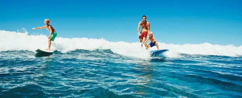 Une famille surfe sur l'océan Atlantique dans les Landes grâce à leur location landes bord de mer
