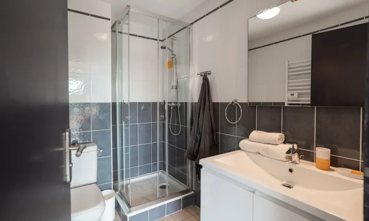 Salle de bain avec WC, douche et lavabo et carrelage blanc et accessoires modernes dans le studio